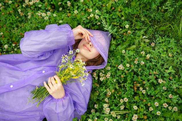 Creative Highlight Symbolbilder Woman in purple raincoat relaxing on grass with wild flowers in summer model released, Symbolfoto, VCF00802