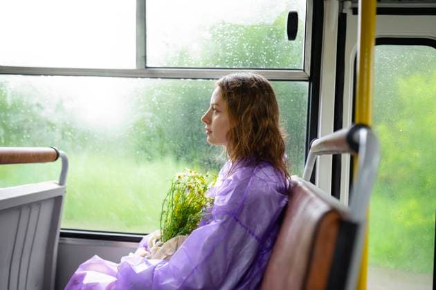 IMAGO Creative, Jahreszeit Sommer, Regen, Sommerregen Creative Highlight Symbolbilder Woman in purple raincoat holding wild flowers sitting on a bus model released, Symbolfoto, VCF00804