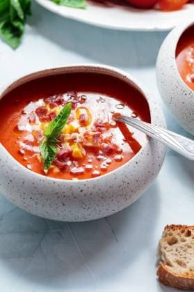 A refreshing bowl of cold tomato soup garnished with chopped egg, ham, and fresh basil. Served in a speckled bowl, it offers a vibrant and appetizing presentation. Model Released EvelynPernas_ID30293_1022180_004 Copyright: xEvelynxPernasx RECORD DATE NOT STATED