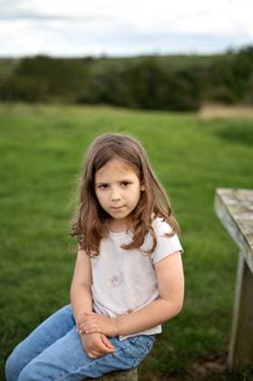 Creative Highlights Symbolbilder Child girl sitting on a wooden bench in a countryside field. Corby, England, United Kingdom R_JNDO250728-1796026-01 ,model released, Symbolfoto