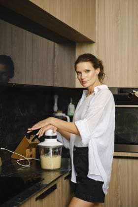Eine Frau steht an einer Küchentheke und mischt Bananen und Sanddornzutaten. Natürliches Licht unterstreicht ihren konzentrierten Ausdruck, während sie einen gesunden Smoothie zubereitet A woman stands at a kitchen counter, blending banana and sea buckthorn ingredients. Natural light highlights her focused expression as she prepares a healthy smoothie Copyright: imageBROKER AlekseixIsachenko ibxfbm14562410.jpg ,model released, Symbolfoto ,property released
