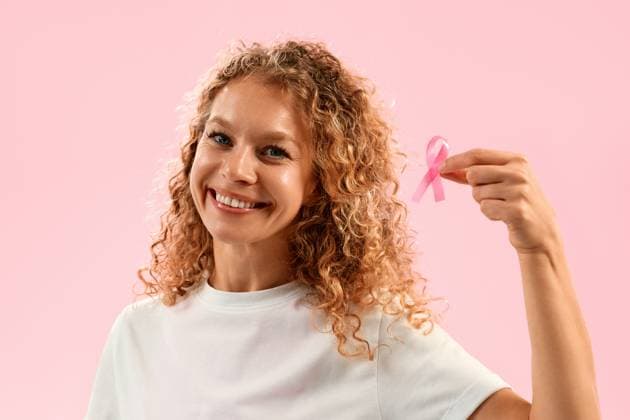 Smiling woman holding pink ribbon on pink background, breast cancer awareness and support concept Happy woman in white shirt smiling and holding pink ribbon on pink background, symbolizing breast cancer awareness, hope, support, and health advocacy concept. Model Released OrionProduction_ID30910_1048099_047 Copyright: xx