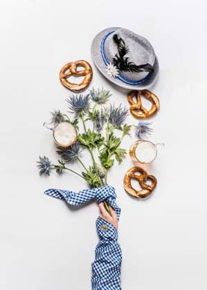 Oktoberfest layout composition with mugs of beer, Bavarian hat with feather, pretzel, woman hand in traditional blue blouse and alpine flowers. Top view. Modern. Flat lay Model Released Vicuschka_ID29975_1012645_015 Copyright: xx