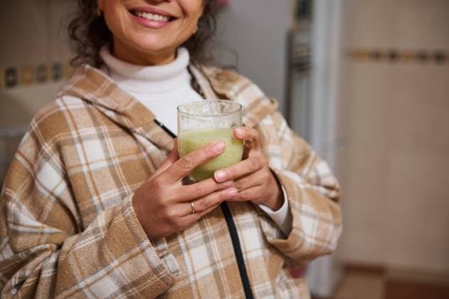 Woman enjoying a healthy green smoothie in cozy kitchen setting Close-up of a smiling woman holding a glass of green smoothie in a cozy kitchen. She wears a warm plaid coat, emphasizing a healthy and comfortable lifestyle., model released, , property released, , 63281452.jpg RECORD DATE NOT STATED