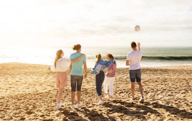 Friends enjoying a sunny day at the beach while playing with a ball A group of five friends stands on the sandy beach, enjoying a sunny day. They are playing with a ball and laughing as the waves crash gently behind them., model released, , 63323714.jpg RECORD DATE NOT STATED
