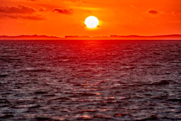 Die untergehende Sonne mit Silhouetten der im Dunst verschwimmenden Gebäude und Bäumen über Sylt vom Strand von Utersum auf der Nordseinsel Föhr aus gesehen Die untergehende Sonne mit Silhouetten der im Dunst verschwimmenden Gebäude und Bäumen über Sylt vom Strand von Utersum auf der Nordseinsel Föhr aus gesehen (License=RF) Copyright: xZoonar.com FrankxWagnerx 23834323