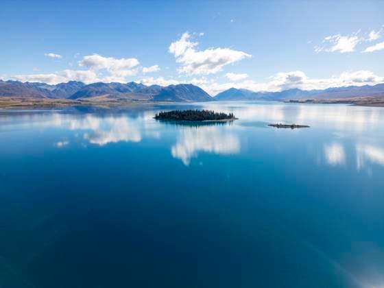 MR_ID30624_22402_JuanAizpuru.jpg Aerial view of Lake Tekapo in Canterbury, New Zealand, showcasing a breathtaking turquoise lake with a small forested island, surrounded by a mountainous landscape. Model Released JuanAizpuru_ID30624_1035975_001 Copyright: xJuanxAizpurux