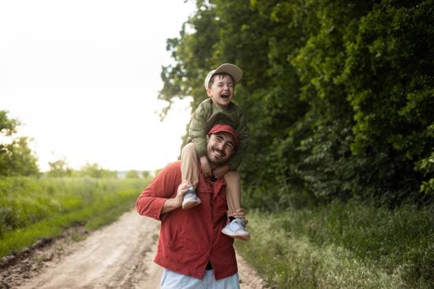 IMAGO Creative, Ostern, Bräuche, Osterspaziergang #2 A joyful dad carrying his son on his shoulders strolls through a lush green field. The pair enjoys the beauty of nature and the warm sunshine during a peaceful afternoon walk. Model Released Ptashkimenko_ID30309_1022971_011 Copyright: xPtashkimenkox RECORD DATE NOT STATED