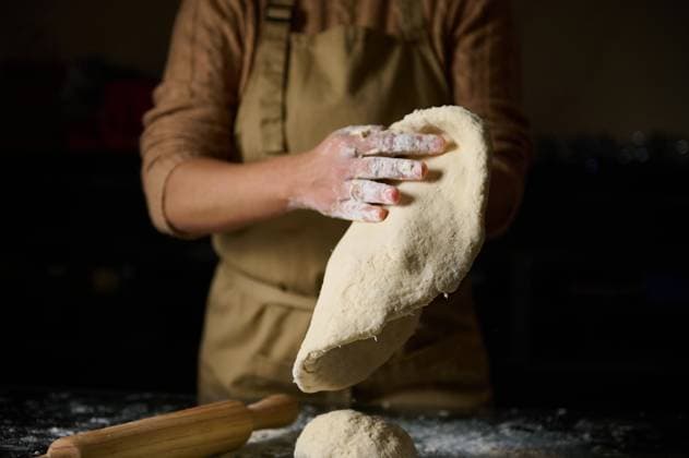 Baker preparing dough by hand in a rustic kitchen setting An individual wearing an apron kneads fresh dough in a dimly lit kitchen, conveying a sense of artisanal baking and culinary craftsmanship., model released, , 63457990.jpg RECORD DATE NOT STATED