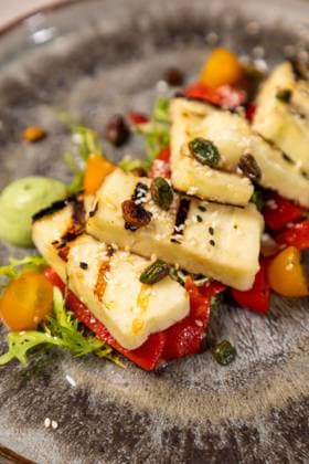 Delicious grilled halloumi cheese salad with a side of pesto sauce Grilled halloumi cheese salad with cherry tomatoes and pistachios being served on a plate, 63074770.jpg RECORD DATE NOT STATED