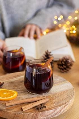 Auf dem Tisch steht ein Glas mit wärmendem Glühwein und eine Frau liest ein Buch. A glass of warming mulled wine is on the table and a woman is reading a book. A cozy autumn day at home. (License=RF) Copyright: xZoonar.com ViktoriiaxPopovax 23870496