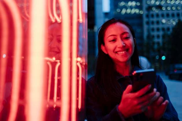 Creative Highlight Symbolbilder Smiling person using smartphone by neon sign in urban setting at night model released, Symbolfoto, ASGF06862