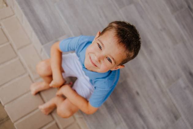 Creative Highlight Symbolbilder Smiling child in blue shirt sitting barefoot on outdoor tile floor model released, Symbolfoto property released, MDOF02973
