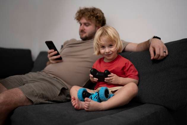 IMAGO Creative, Lifestyle, Gaming Father and son relaxing at home playing video game on sofa model released, Symbolfoto property released, OGSF00215