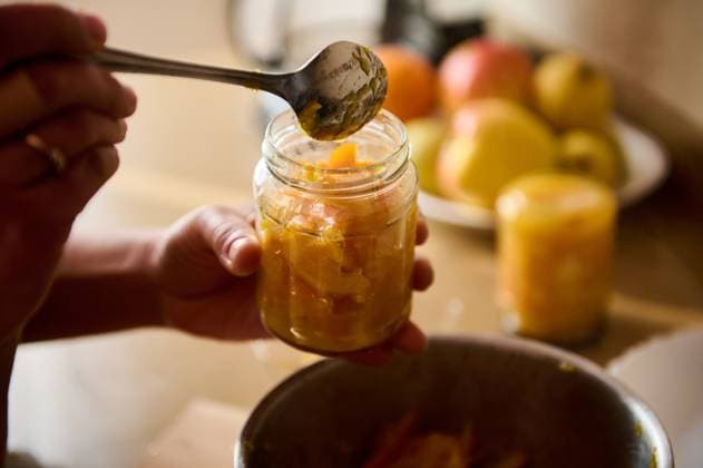 Person preserving sliced fruit in jars in a bright kitchen setting Hands carefully filling glass jars with sliced fruit and spices, preparing homemade preserves in a kitchen. A background of fresh ingredients creates a warm and productive atmosphere., model released, , 64475914.jpg RECORD DATE NOT STATED