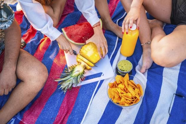 Freunde machen ein Picknick auf einem gestreiften Handtuch, schneiden Ananas, haben Wassermelone, Nachos, Guacamole und Saft dabei Friends are having a picnic on a striped towel, cutting pineapple, with watermelon, nachos, guacamole, and juice nearby Copyright: imageBROKER UnaixHuizi ibxuhu14448365.jpg ,model released, Symbolfoto ,property released