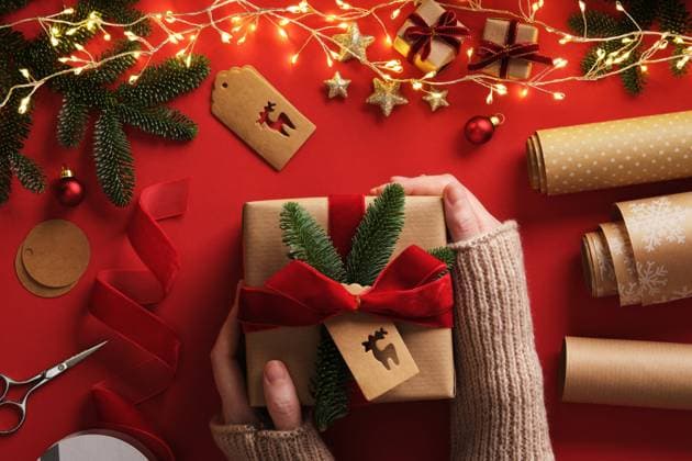 A woman s hands hold a wrapped gift. Table with handmade items, rolls of kraft brown paper, red velvet ribbon, labels, scissors. A woman s hands hold a wrapped gift. Table with handmade items, rolls of kraft brown paper, red velvet ribbon, labels, scissors., 64084110.jpg RECORD DATE NOT STATED