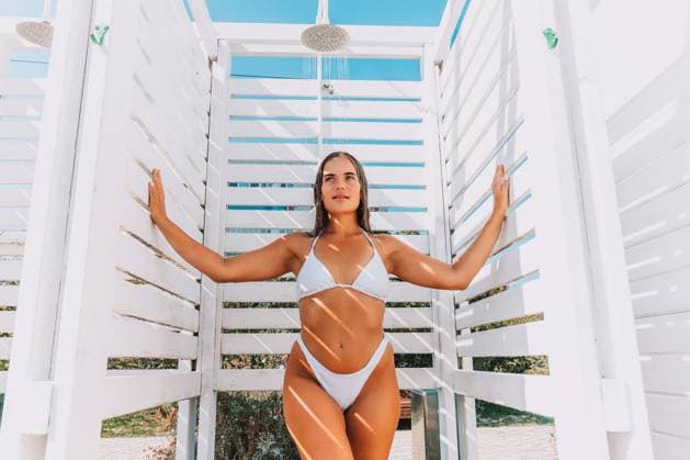 A woman in a bikini poses in front of a white structure with a shower. She is holding a glass of wine and she is enjoying herself A woman in a bikini poses in front of a white structure with a shower. She is holding a glass of wine and she is enjoying herself., model released, , 63310008.jpg RECORD DATE NOT STATED