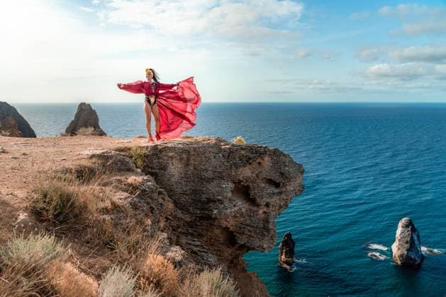 A woman in a red dress stands on a rocky cliff overlooking the ocean. The scene is serene and peaceful, with the woman s flowing dress adding a sense of grace and beauty to the landscape. A woman in a red dress stands on a rocky cliff overlooking the ocean. The scene is serene and peaceful, with the woman s flowing dress adding a sense of grace and beauty to the landscape, model released, , property released, , 63348550.jpg RECORD DATE NOT STATED