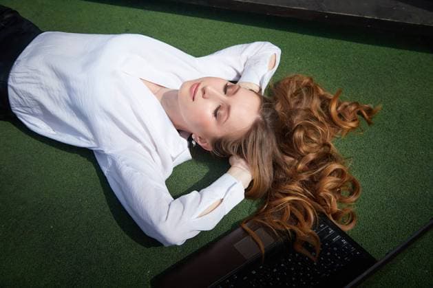 Relaxing outdoors, a young woman lounges on green grass with a laptop nearby on a sunny day A young woman with long curly hair enjoys a moment of relaxation on green grass, surrounded by sunshine and a laptop., model released, , 95621448.jpg RECORD DATE NOT STATED