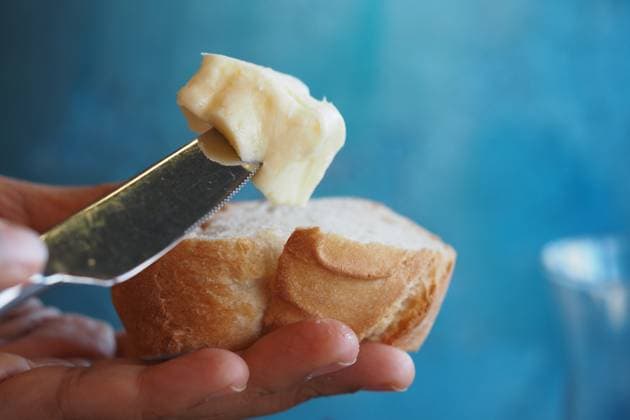 Spreading creamy butter on fresh bread with a blue backdrop A hand applies soft butter on a slice of bread against a blue background., 65042114.jpg RECORD DATE NOT STATED