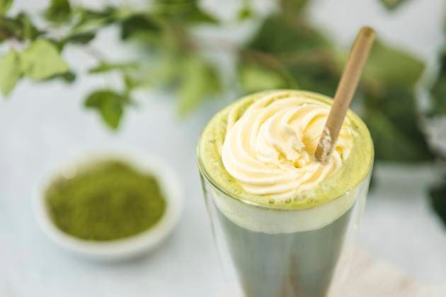 Matcha latte with whipped cream and powdered tea in a glass Glass of matcha latte topped with whipped cream and accompanied by powdered green tea on a blurred background with green leaves, 94703966.jpg RECORD DATE NOT STATED
