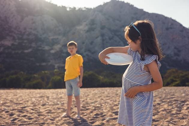 Children playing with frisbee on a sunny beach day A girl in a striped dress and a boy in a yellow shirt enjoy playing with a frisbee on a sandy beach. The sunny backdrop features rugged mountains and blue skies Model Released AlinaKandybka_ID31083_1054465_003 Copyright: xAlinaxKandybkax RECORD DATE NOT STATED