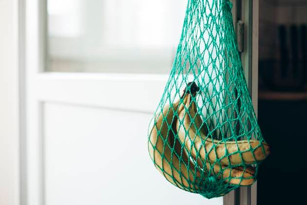 Hanging bananas in eco-friendly green mesh bag Fresh bananas hang in a reusable, eco-friendly green mesh bag against a bright kitchen setting. The natural light highlights the texture and promotes sustainable living Model Released HannaYakimenko_ID31199_1058823_013 Copyright: xHannaxYakimenkox