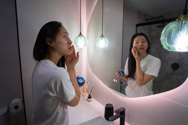 Woman applying skincare cream during morning routine An asian woman calmly applies skincare cream in front of a mirror, illustrating a serene morning routine. The ambient lighting enhances the peaceful, self-care atmosphere Model Released JuanAlbertoRuiz_ID30776_1042654_008 Copyright: xJuanxAlbertoxRuizx RECORD DATE NOT STATED
