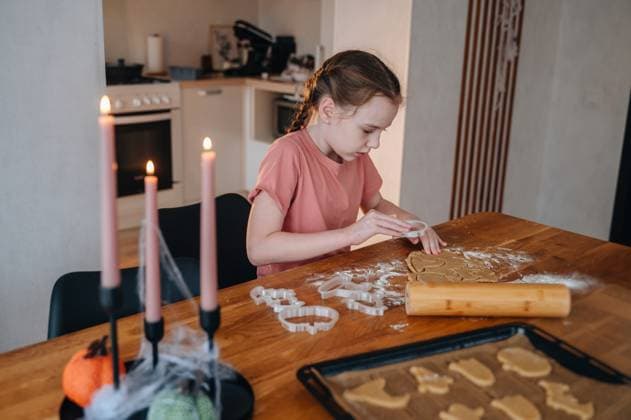 MR_ID31323_22623_LizaPrimak.jpg A young girl is using cookie cutters to shape dough into spooky Halloween cookies. The table is decorated with candles and festive items, creating a warm atmosphere. Model Released KatrinPrimak_ID31323_1064967_002 Copyright: xKatrinxPrimakx