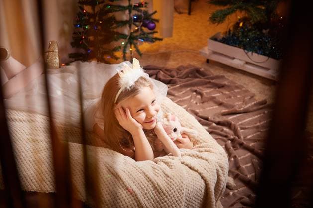 Holiday celebration with child enjoying Christmas decorations and gifts in cozy indoor setting A joyful child relaxes on a blanket while admiring Christmas decorations and gifts, surrounded by festive lights., model released, , 96639238.jpg RECORD DATE NOT STATED