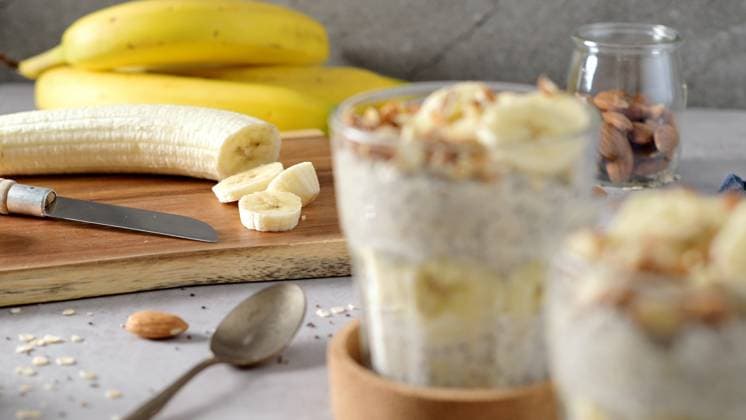 IMAGO Creative, Food, High Protein Frühstück Two bowls of overnight oats topped with banana slices and almonds Two bowls of overnight oats topped with banana slices and almonds. A spoon, cutting board, knife, and a blue napkin rest nearby., 63441024.jpg RECORD DATE NOT STATED