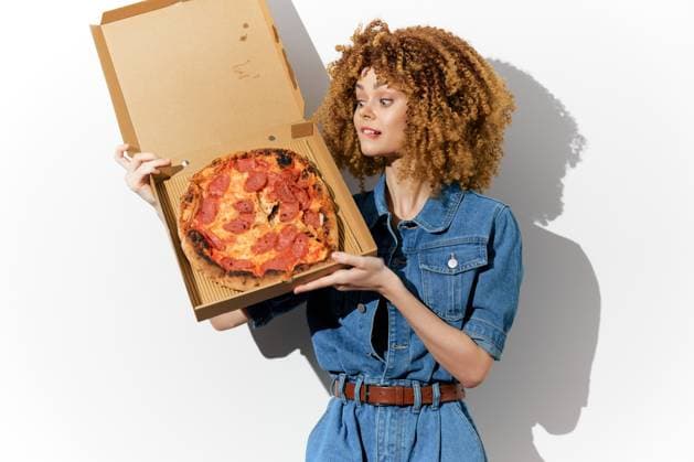 Young woman with curly hair holding a pizza box, showcasing vibrant fast food in a casual denim outfit against a clean, white background A cheerful young woman with curly hair presents an appetizing pepperoni pizza in a cardboard box, wearing a denim outfit The bright, white background highlights the joyful fast food concept, model released, , 97032422.jpg RECORD DATE NOT STATED