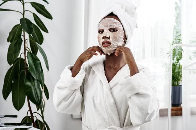 Relaxing spa day at home with a facial mask treatment in a bright and serene environment Woman wearing a facial mask applies it while in a cozy robe. She sits in a well-lit space with indoor plants, enjoying her self-care routine during the morning., model released, , 97513494.jpg RECORD DATE NOT STATED
