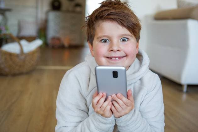 Germany - September 17, 2025: PHOTOMONTAGE, A child sits enthusiastically in the living room with a smartphone in their hand. The image shows digital media use in everyday life, entertainment, and the strong influence of technology on children. Digitally edited. *** FOTOMONTAGE, Ein Kind sitzt begeistert im Wohnzimmer mit einem Smartphone in der Hand. Das Bild zeigt digitale Mediennutzung im Alltag, Unterhaltung und den starken Einfluss von Technik auf Kinder. Digital nachbearbeitet.