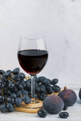 Ein Glas Rotwein mit Trauben und Feigen auf einem Holzbrett, heller Hintergrund A glass of red wine with grapes and figs on a wooden board, light-coloured background Copyright: imageBROKER LucasxSeebacher ibxlse15129451.jpg