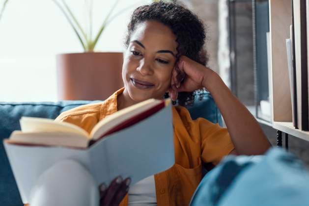 Smiling woman relaxing on sofa at home while reading a book model released, Symbolfoto property released, JSRF03977