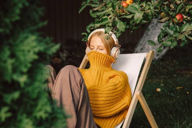 Woman relaxing outdoors listening to music under apple tree in autumn model released, Symbolfoto, VSNF04097
