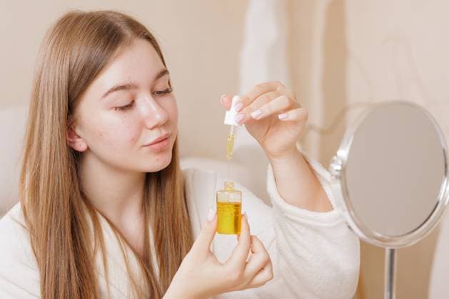 Young Woman Applying Facial Oil Serum with Dropper for Skin and Hair Care Beauty Routine at Home Portrait of woman applying facial oil serum with dropper for skin and hair care in home beauty routine, model released, , 98032018.jpg RECORD DATE NOT STATED
