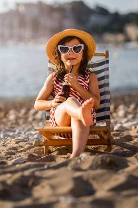 Creative Highlight Symbolbilder MR_ID31274_22583_MayaBosquetCarli.jpg, MR_ID31274_22584_LeoBosquetCarli.jpg A cute little girl relaxes in swimwear on a sandy beach during summer vacation. She sits in a deck chair, wearing a sun hat and sunglasses, sipping a drink. Model Released MagdalenaCarli_ID31274_1062187_003 Copyright: xMagdalenaxCarlix