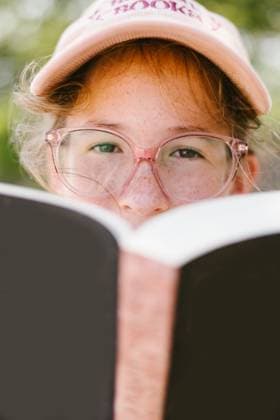 Brown eyed girl with glasses looks at camera over top of book Beach Park, Illinois, United States CR_WVNP250925B-1831545-01 ,model released, Symbolfoto