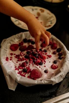 Hand adding frozen berries on creamy yogurt dessert Amsterdam, North Holland, Netherlands CR_RTBZ25093082-1843935-01