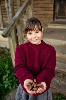 Child girl in a red sweater holding acorns near wooden house. Corby, England, United Kingdom R_JNDO251003A-1844588-01 ,model released, Symbolfoto