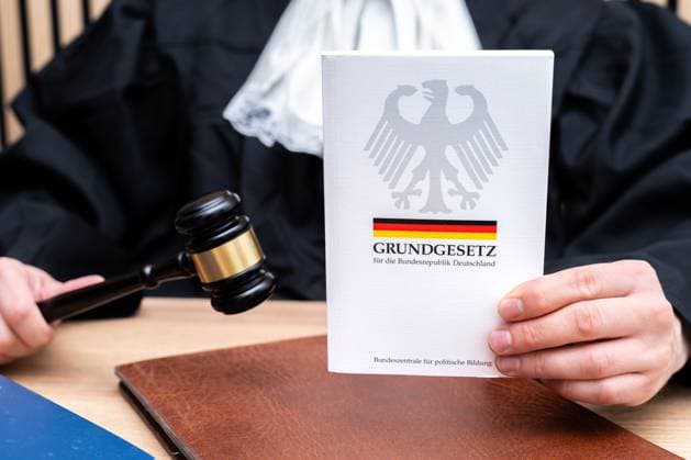Bavaria, Germany - October 8, 2025: A judge holds the Basic Law of the Federal Republic of Germany in his hand. The symbolic photo stands for the rule of law, the constitution, democracy and the importance of the Basic Law in the Federal Republic of Germany *** Ein Richter hält das Grundgesetz der BRD in der Hand. Das Symbolfoto steht für Rechtsstaat, Verfassung, Demokratie und die Bedeutung der Grundgesetze in der Bundesrepublik Deutschland