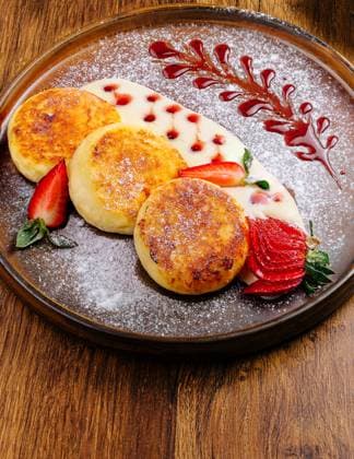 IMAGO Creative, Food, High Protein Frühstück Leckere Hüttenkäsepfannkuchen mit Sahne, Beeren und Puderzucker A gourmet dining experience showcases a vibrant plate of pancakes adorned with strawberries, a succulent burger alongside fries, and colorful grilled skewers on a wooden table. (License=RF) Copyright: xZoonar.com AntonxDobreax 24013477