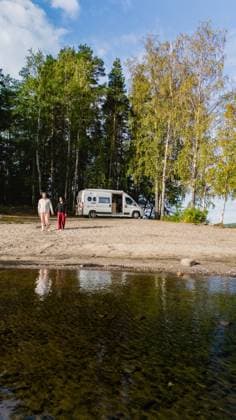 Einen ruhigen Tag am Saimaa-See in Finnland mit einem Wohnmobil und der Natur genießen Two individuals stroll along the sandy shore of Lake Saimaa in Finland, with a camper van parked nearby. Vibrant greenery surrounds the serene waters, creating a tranquil atmosphere. (License=RF) ,model released, Symbolfoto Copyright: xZoonar.com FokkexBaarssenx 24051661 ,model released, Symbolfoto ,property released
