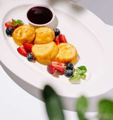 Leckeres Frühstücksgericht mit Käsepfannkuchen und frischen Beeren A platter displays golden cheese pancakes arranged neatly alongside strawberries, blueberries, and a rich berry sauce. (License=RF) Copyright: xZoonar.com AntonxDobreax 24061865