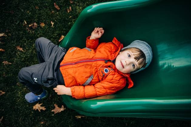 Child in orange coat lying calmly on green slide outdoors North Andover, Massachusetts, United States CR_FKNH251013B-1850455-01 ,model released, Symbolfoto
