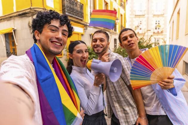 Gruppe verschiedener junger Menschen, die lächeln und die Gay Pride Bewegung feiern, während sie eine Regenbogenflagge, ein Megaphon und einen bunten Handfächer auf einer Straße in der Stadt halten Group of diverse young people smiling and celebrating gay pride movement while holding a rainbow flag, a megaphone, and a colorful hand fan in a city street Copyright: imageBROKER UnaixHuizi ibxuhu15317578.jpg ,model released, Symbolfoto ,property released