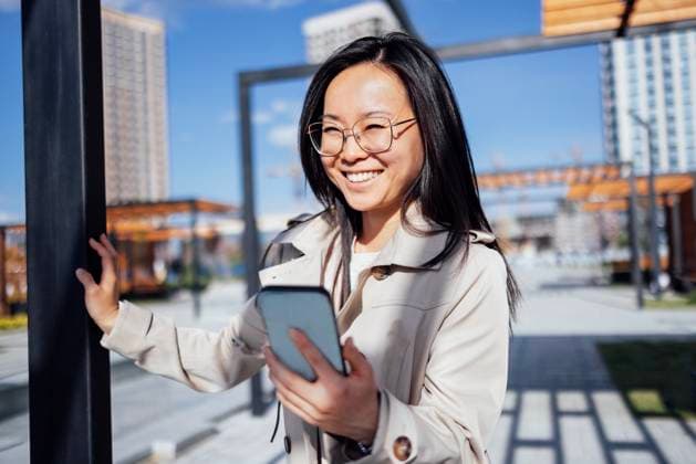 Eine junge asiatische Frau mit Brille lächelt und schaut auf ein Telefon auf der Straße. Ein Koreaner lacht und hält ein Handy vor dem Hintergrund einer Stadtlandschaft. A young Asian woman in glasses smiles and looks at a phone on the street. A Korean laughs and holds a mobile against the background of an urban landscape. A girl in a coat uses a smartphone outdoors (License=RF) ,model released, Symbolfoto Copyright: xZoonar.com DashaxPetrenkox 23944752 ,model released, Symbolfoto ,property released